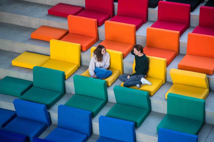 Two students sitting in a group of rainbow colored chairs