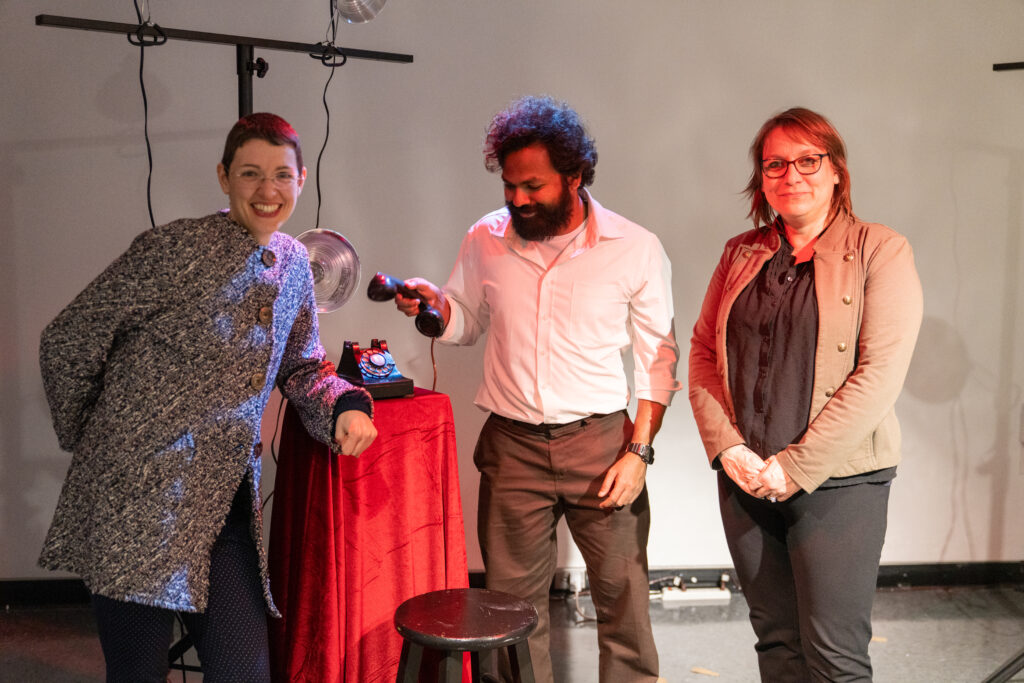 Three people stand together with one holding a microphone