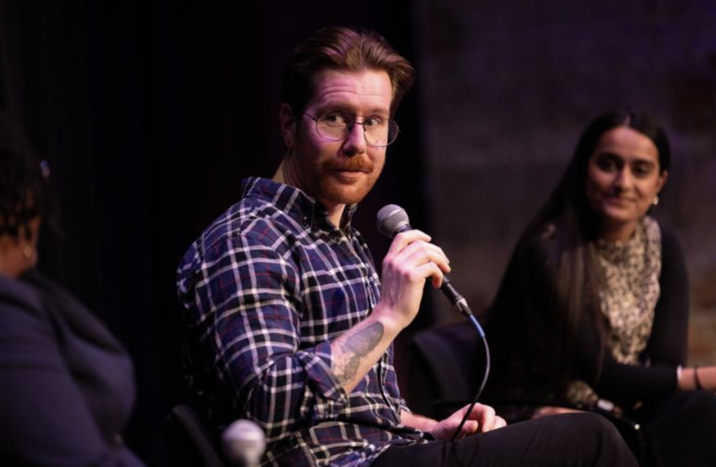 A person holds a microphone while talking and sitting