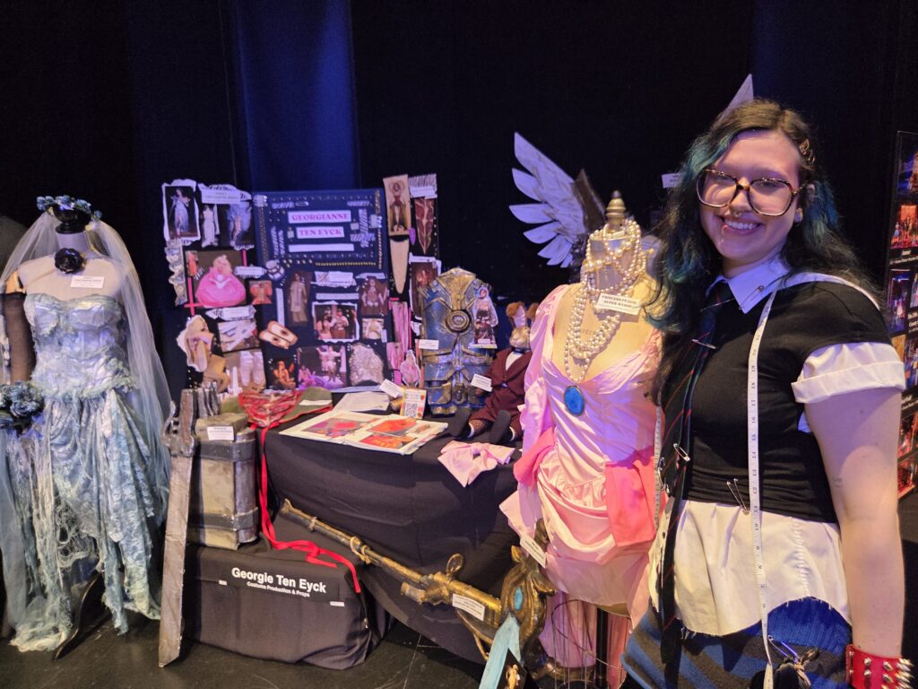A person stands near their designed costumes