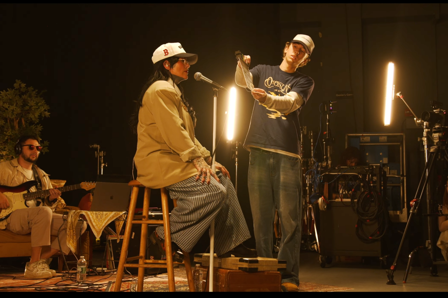 An assistant with a film clapper stands in front of Lisa Bello, seated on a stool.