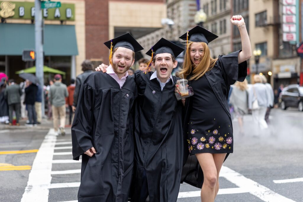 Three students pose in a crosswalk in their caps and gowns||||||||||||||||||