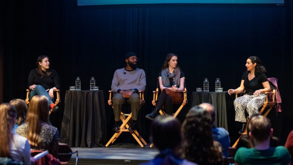 Four panelists seated in directors' chairs on a stage||