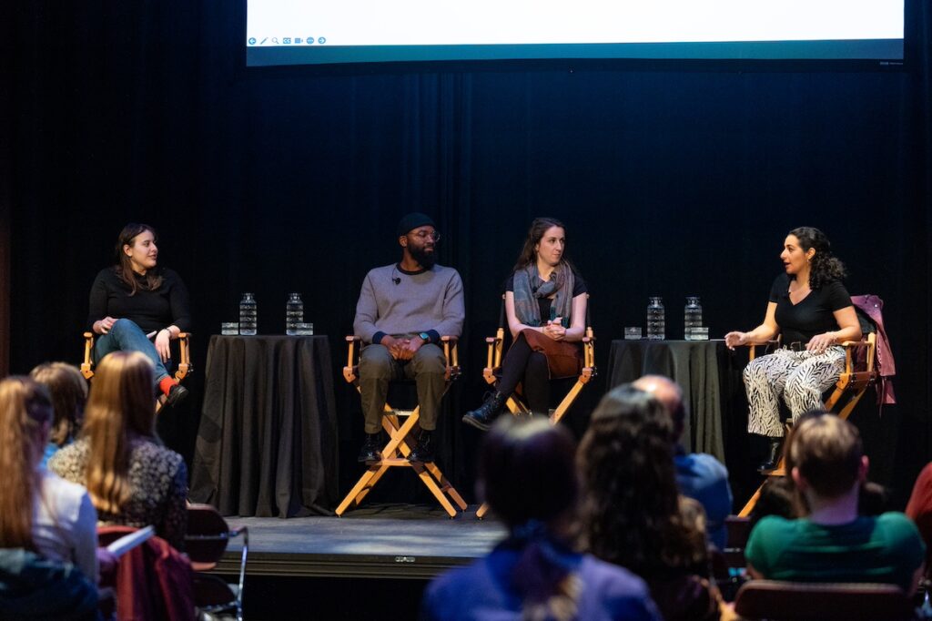 Four panelists seated in directors' chairs on a stage||