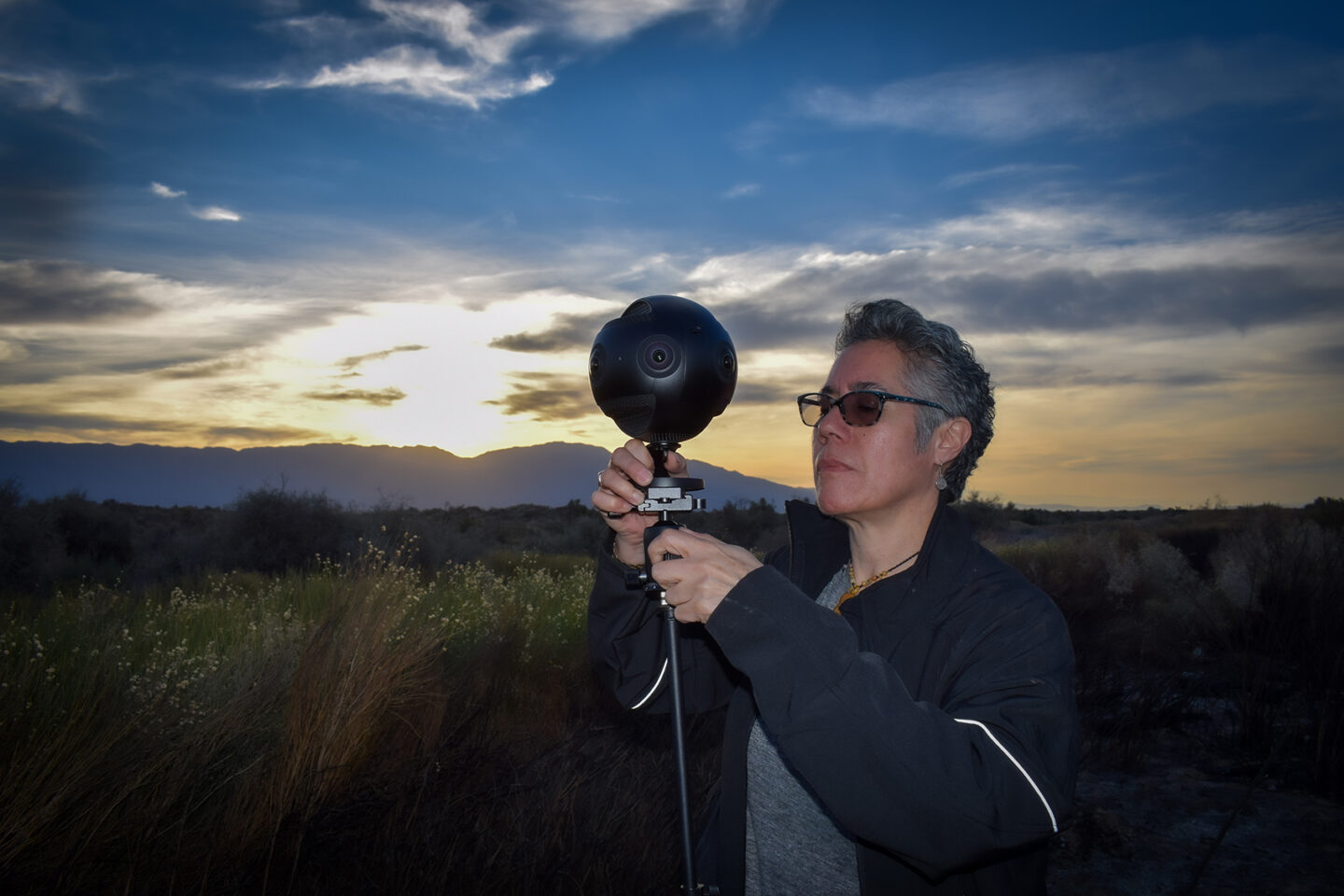 cristina adjusting camera in field at dusk|woman in coat