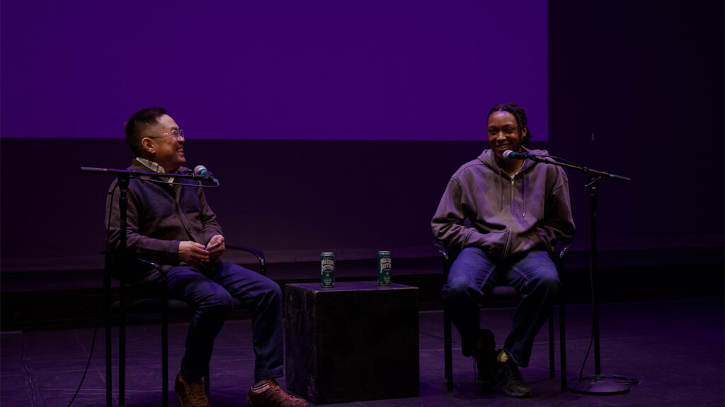 Josh Johnson and Ed Lee speak to each other on stage while sitting in chairs|||