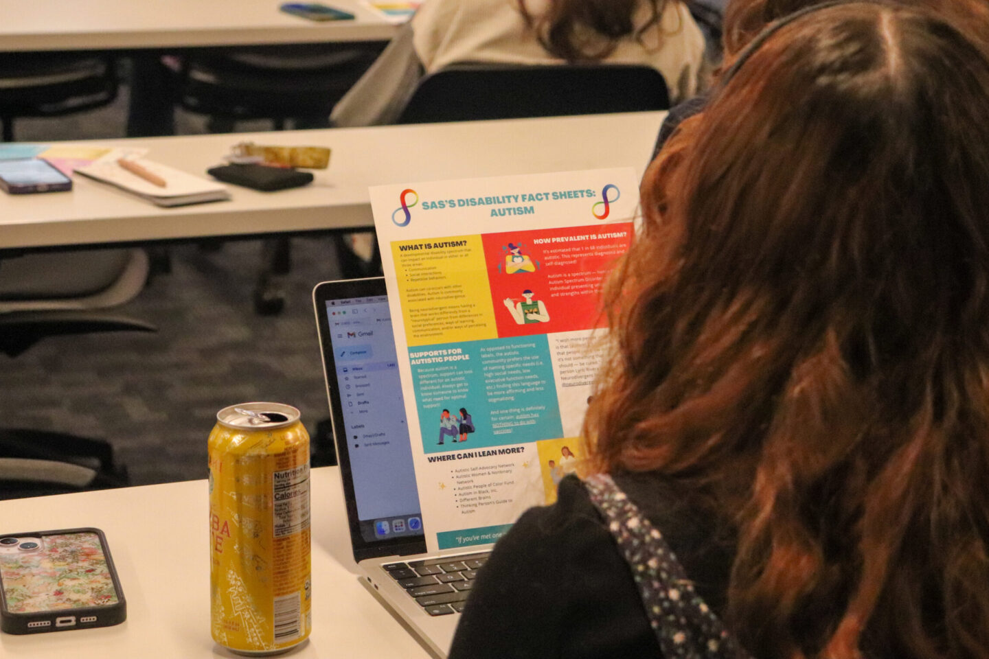 The back of a panel attendee is shown staring at a colorful handout. The handout is a resource on autism and the prevalence of neurodivergency nationally and worldwide.|Dr. Lisa Wisman Weil talks and gestures as Karli Wallace and Melina List look on. A rainbow presentation screen is in the background.||Melina List sits in the center of the panel