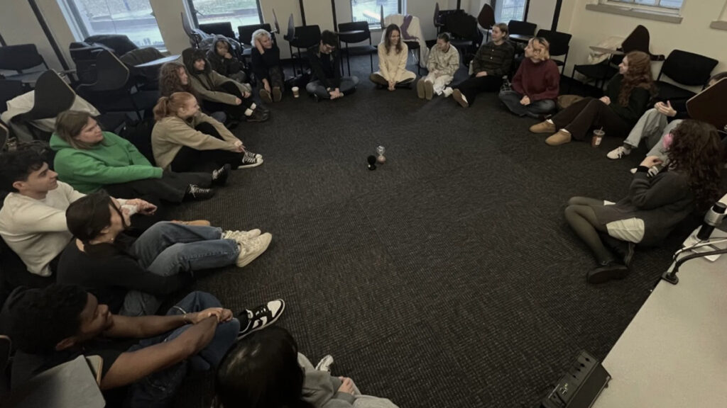Students sit on the floor in a circle||