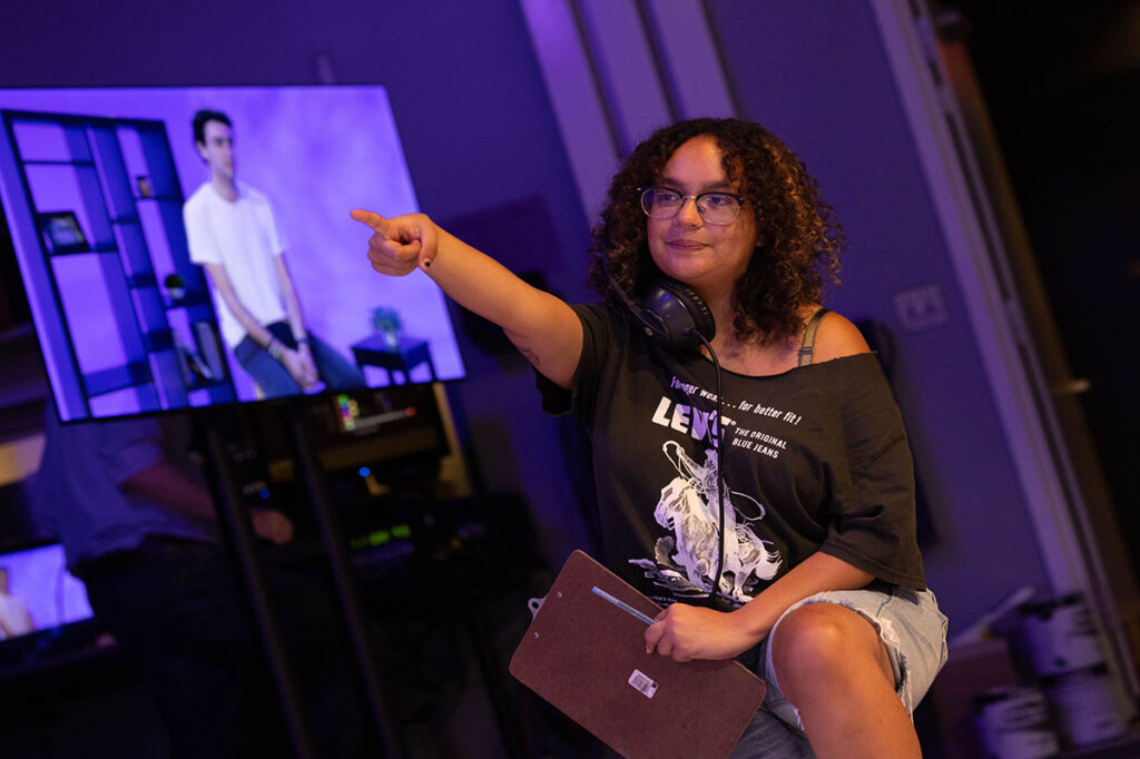 |Behind the scenes of a TV production|A student points while directing a TV production|A student works with lighting equipment|A student looks at a TV camera|Paul Turano teaches analog film to several students