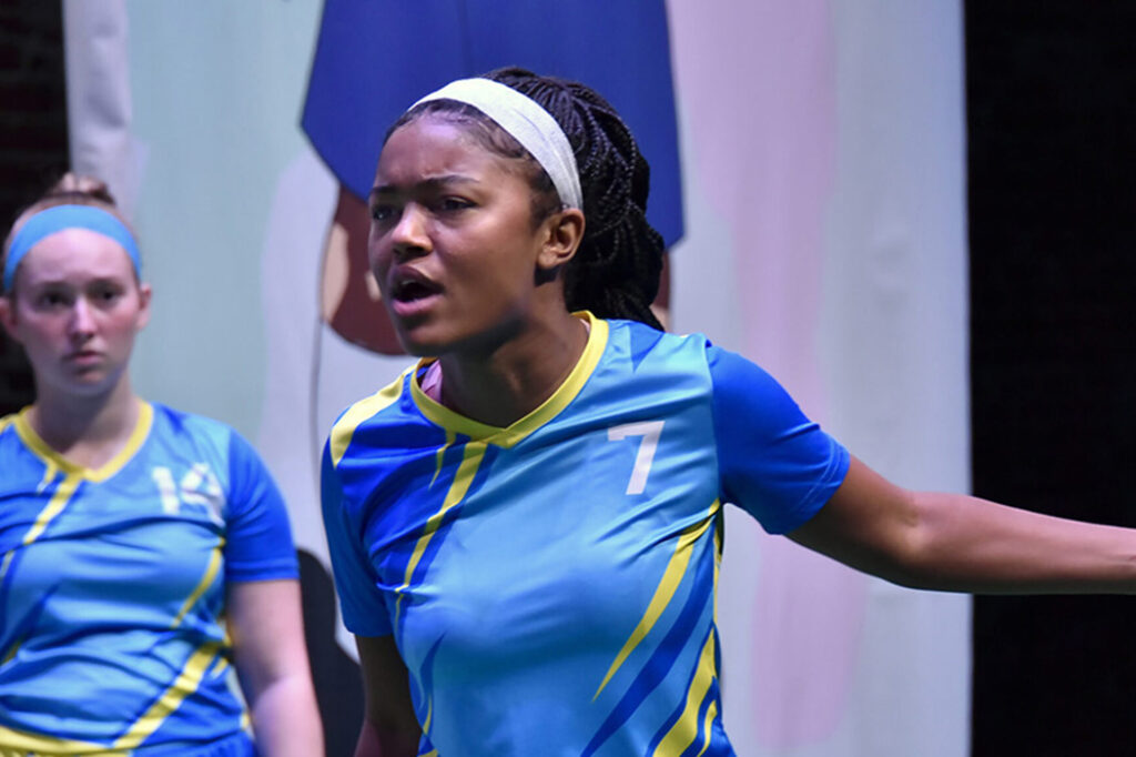 Woman in soccer uniform gestures on stage||||Promotional poster for Stranger Things: The First Shadow|Woman in soccer uniform gestures on stage
