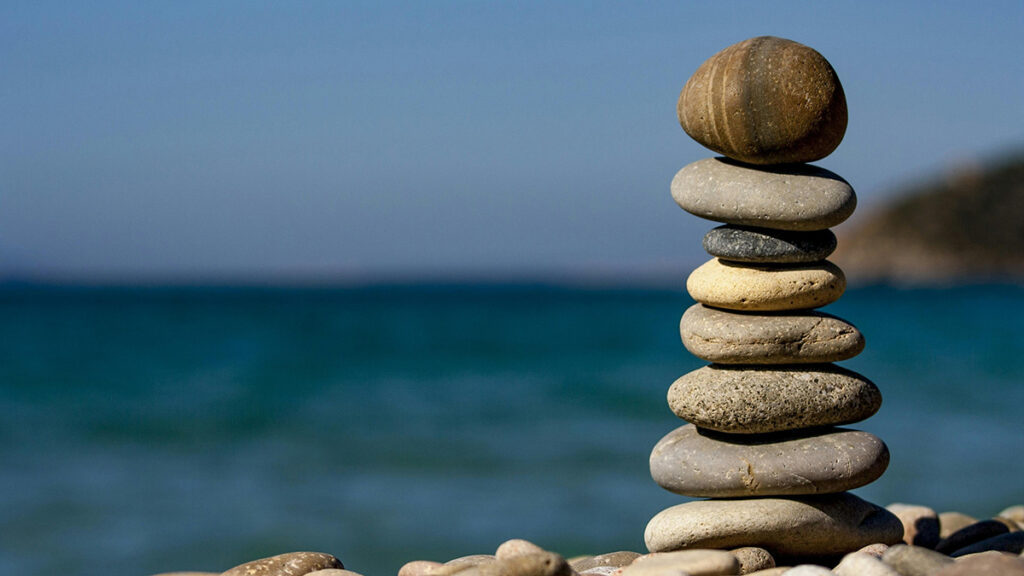 rocks balanced in a stack next to sea|woman with blonde bob wearing black suit sits looking off camera||colorful game pieces connected by lines