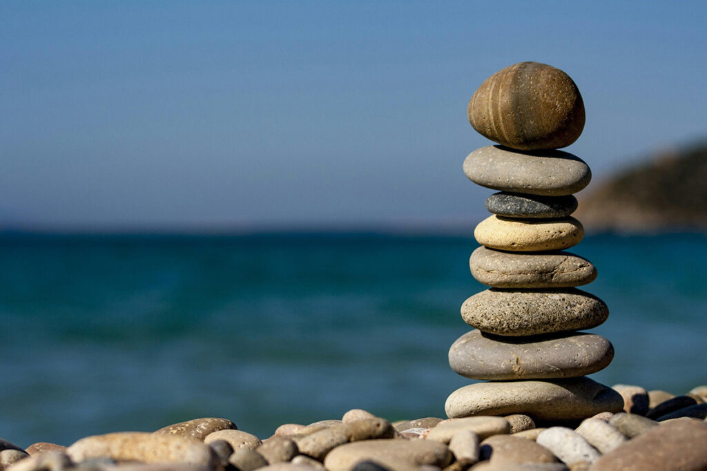 rocks balanced in a stack next to sea|woman with blonde bob wearing black suit sits looking off camera||colorful game pieces connected by lines