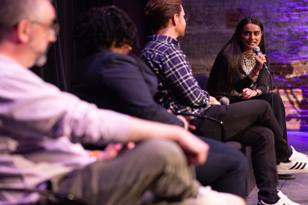 Diti Kohli moderates a panel discussion|Bridgit Brown speaks while Nicholas Medvescek looks at her|Greg Almeida speaks while standing|Diti Kohli moderates a panel discussion while everyone sits in chairs||Nicholas Medvescek speaks while holding a microphone and sitting|The view is of the audience looking at a man standing in front of a lectern from behind the man