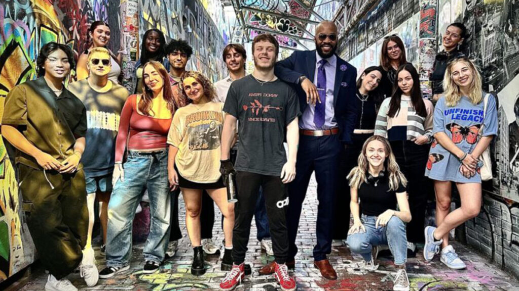 Jae Williams standing in heavily graffitied space surrounded by students|||||||||