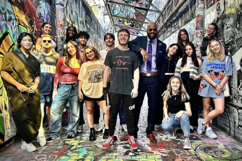 Jae Williams standing in heavily graffitied space surrounded by students|||||||||
