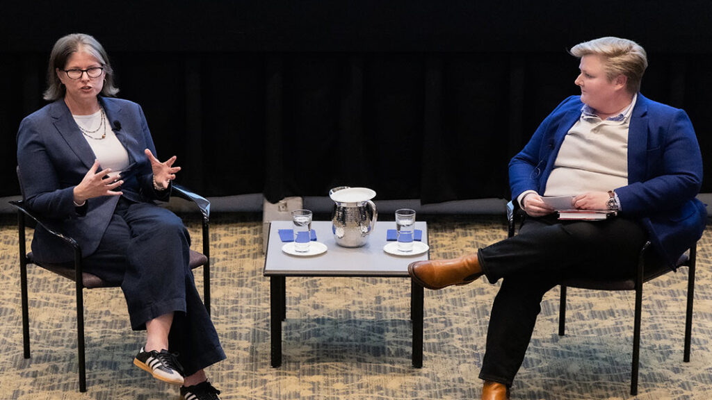 Jane McManus sits in a chair while speaking with Mary Ann Taylor