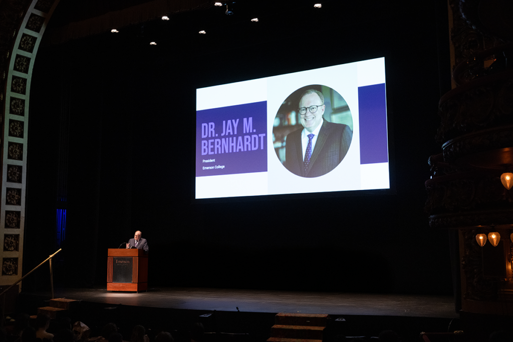 Man speaks at podium in corner of the stage as image is projected above