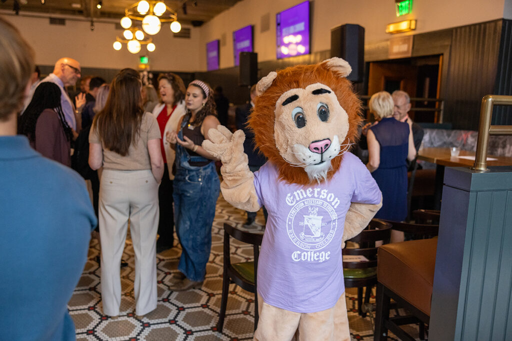 Person in lion costume and Emerson t-shirt waves at gathering