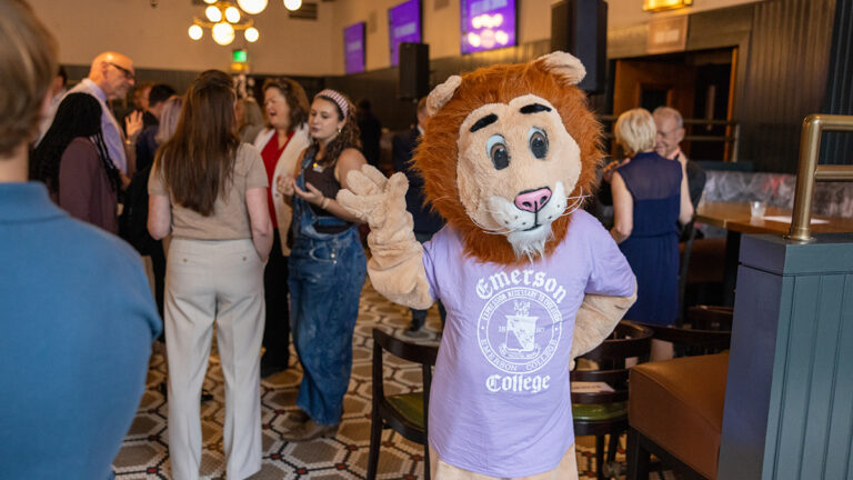 Person in lion costume and Emerson t-shirt waves at gathering