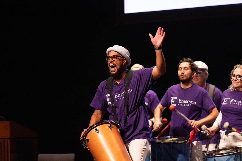 People in purple t-shirts play drums on stage