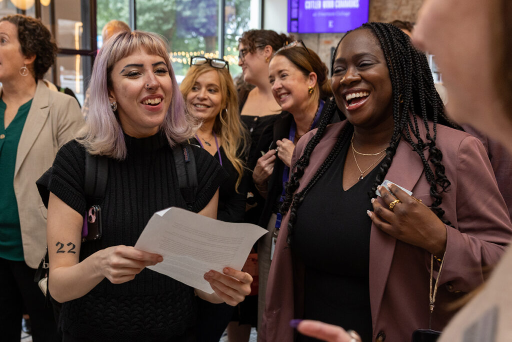 Woman holding piece of paper laughs with woman standing next to her