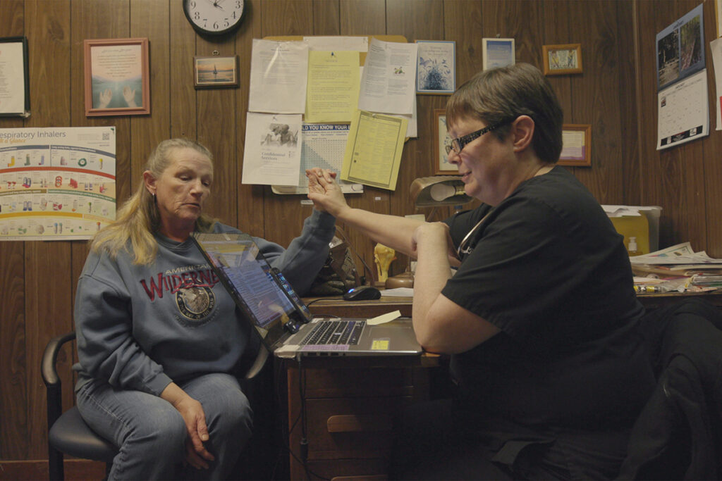 Dr. Kinsell sits in dark office, high fiving female patient in grey sweatshirt