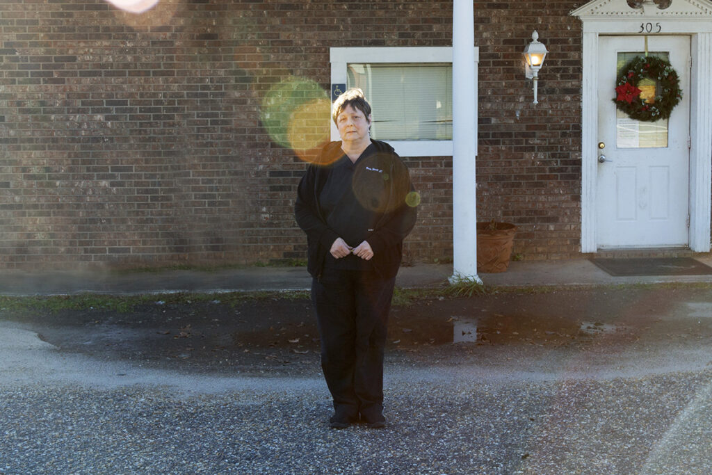 Dr. Kinsell stands in front of a small brick building with a Christmas wreath on the door