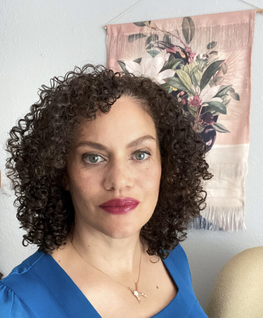 Kirsten Imani Kasai in blue top in front of pink floral wall hanging