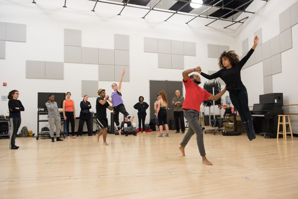 A person helps another person leap in a dance studio