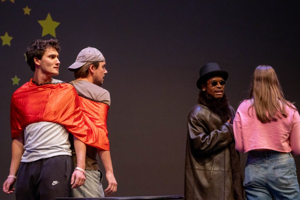 Two people are wrapped together while two other people talk on stage