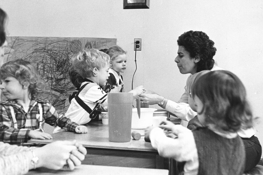 Woman sits across table from small child wearing hearing aid