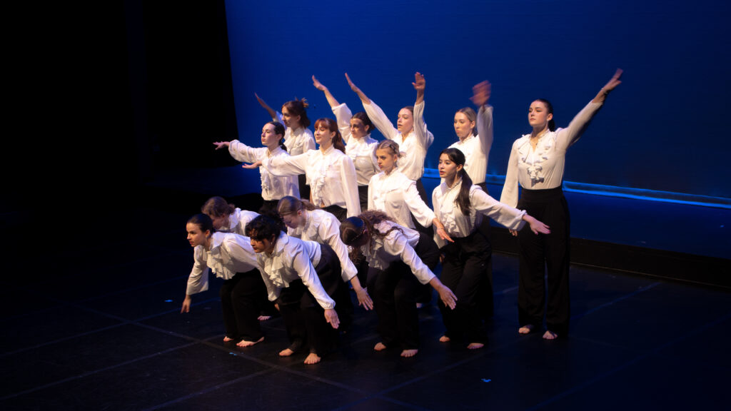 Some dancers are leaning down, some are standing up high with arms extended