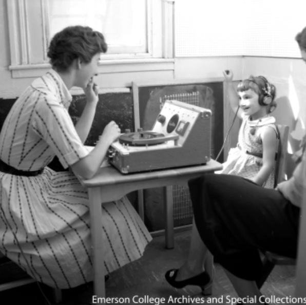 A young girl raises her right hand during an auditory test provided by a clinician