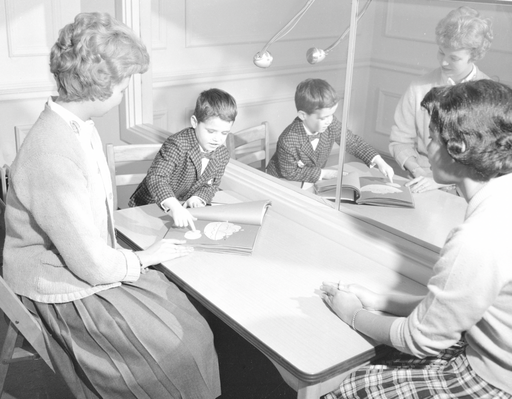A boy points out something on the table in front of two clinicians