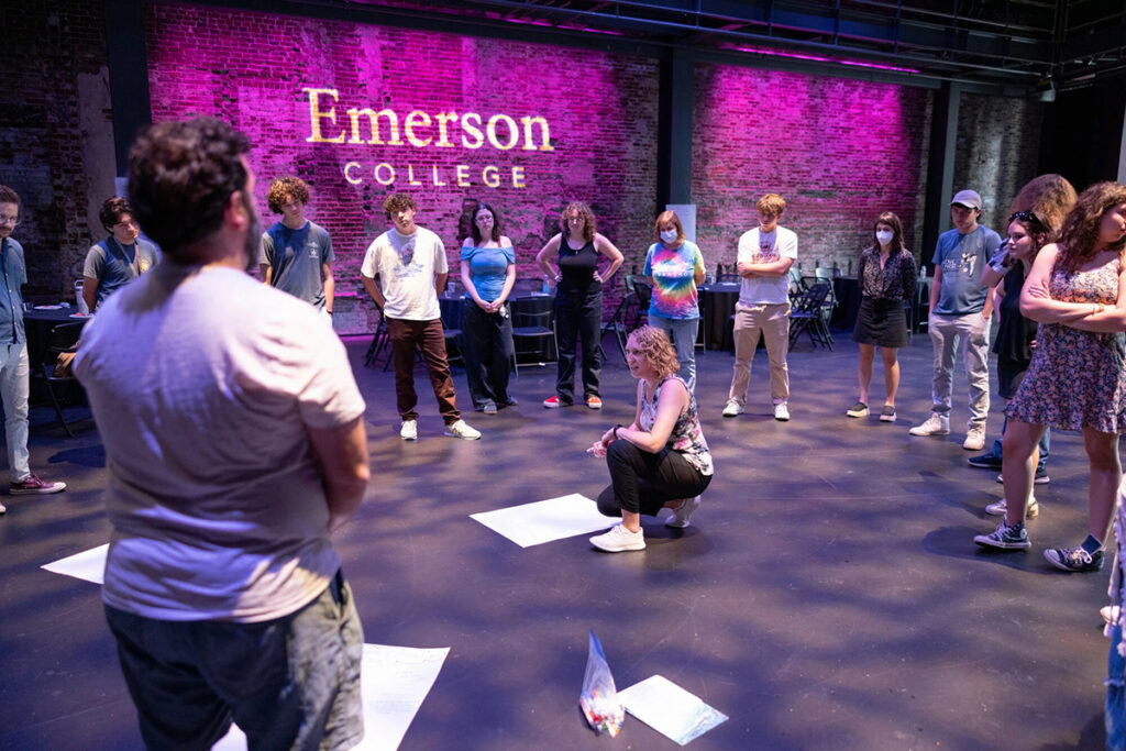 woman kneels in front of large piece of paper as people stand around her in circle