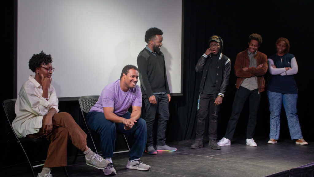 Two people sit in chairs while four people stand on stage