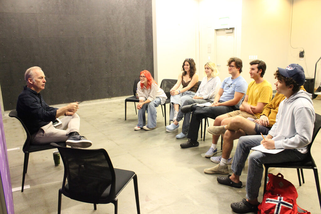 Bob Odenkirk sits in chair speaking to students in chairs in classroom