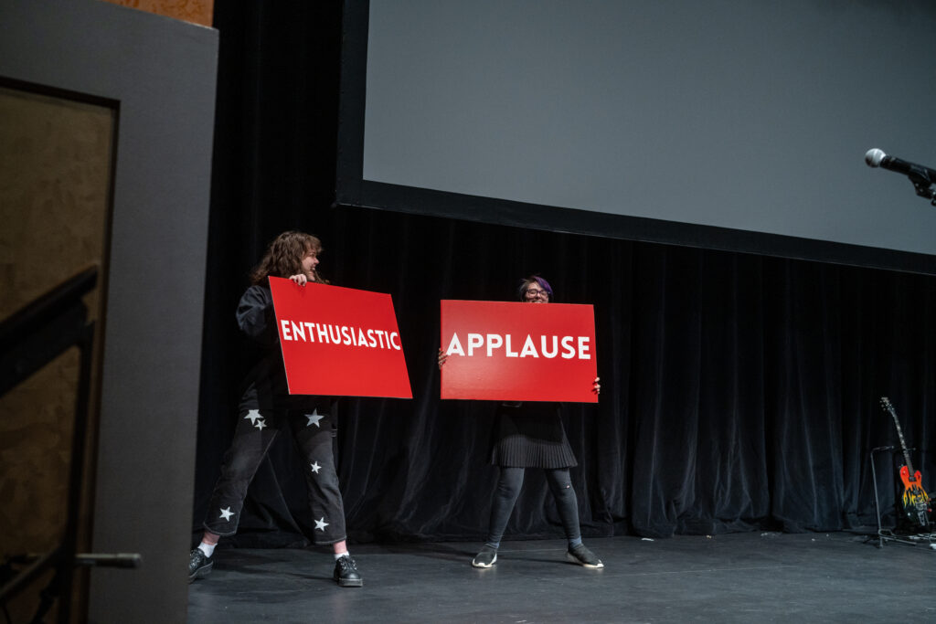 Two people hold up signs that read: Enthusiastic Applause