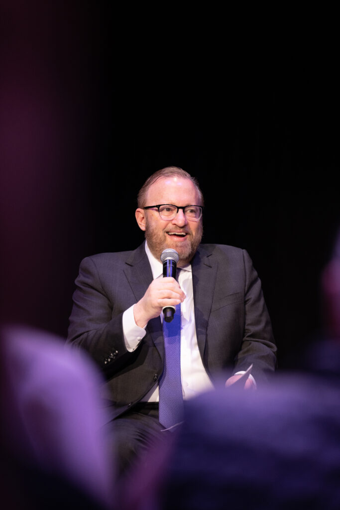 Jay Bernhardt smiles while speaking and holding a microphone