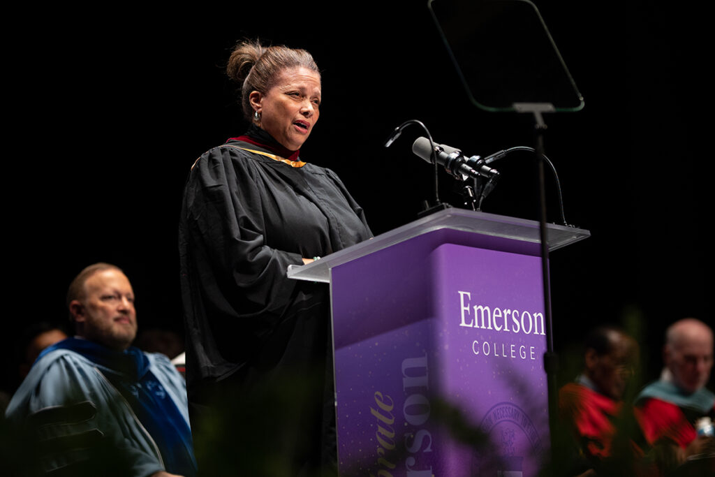 Woman in black robe speaks at podium as President Bernhardt looks on