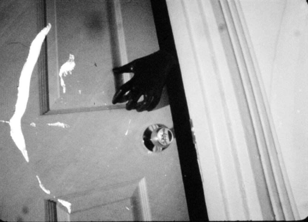 A black hand reaches behind a door