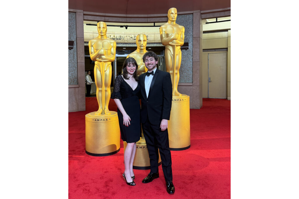 Ruby Brooks with Michael Kiaunis standing in front of three life size Academy Awards
