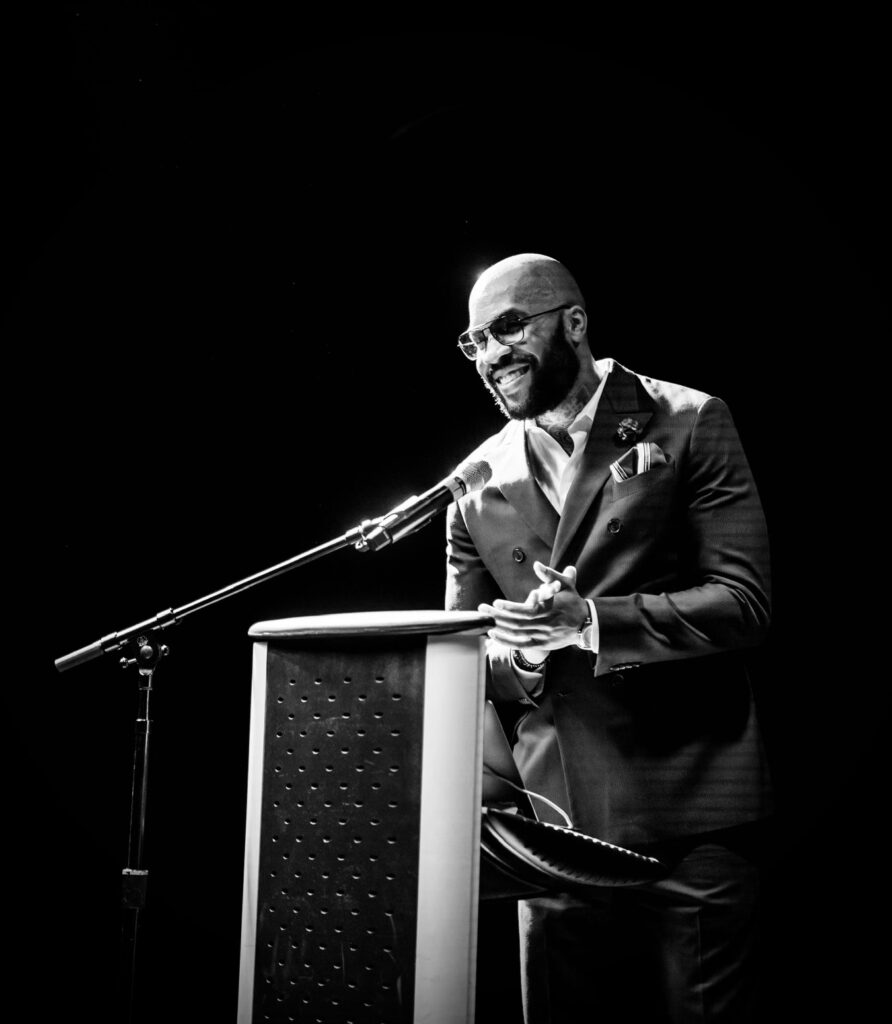 Jae Williams stands by a lectern with a microphone in front of him