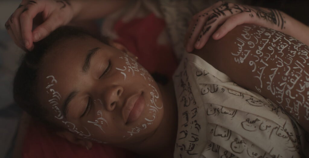 A girl with arabic written on her arms and face lies with her eyes closed