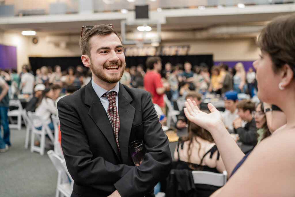 A person in a suit and tie smiles while talking to someone 
