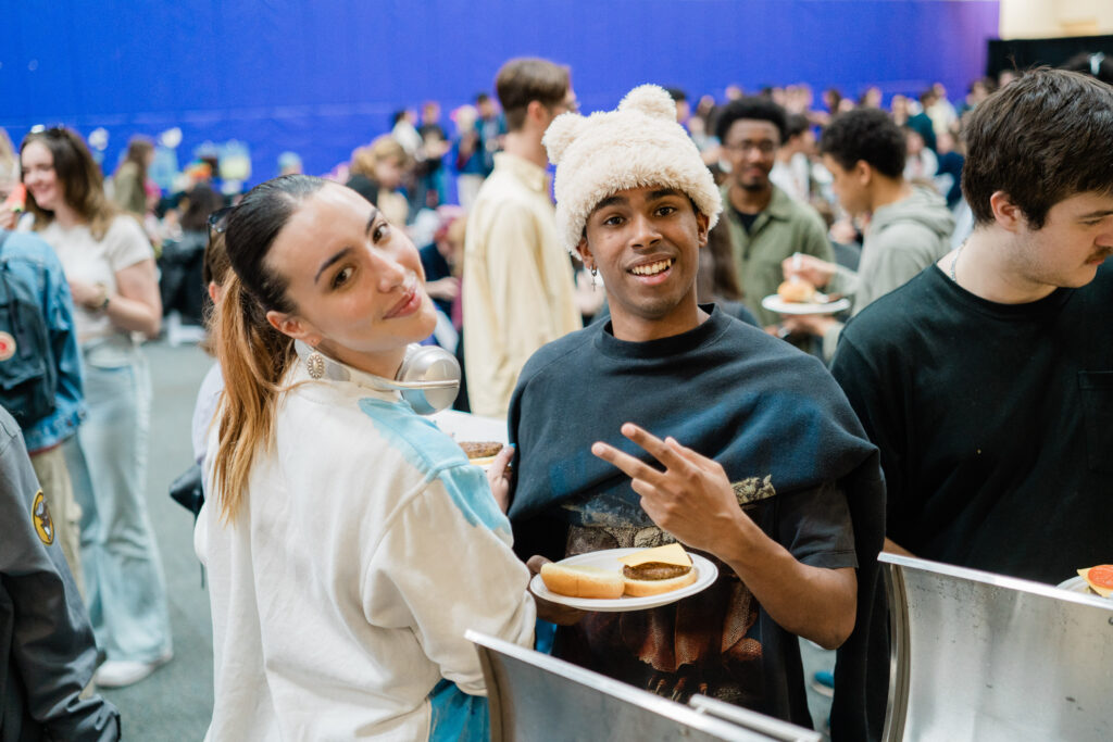 Two people stand next to each other, one holding a plate of food