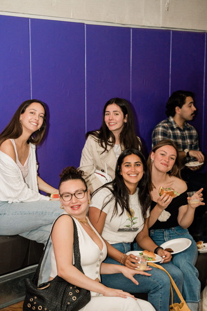 Five people look at the camera while sitting with plates of food