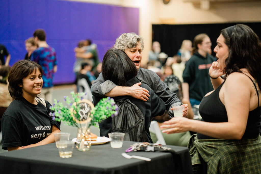 A faculty member hugs one person while two other people look at each other and smile