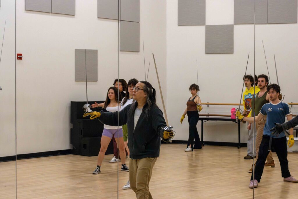 Looking at a mirror's reflection of Ted Hewlett with a sword, teaching his class about sword play