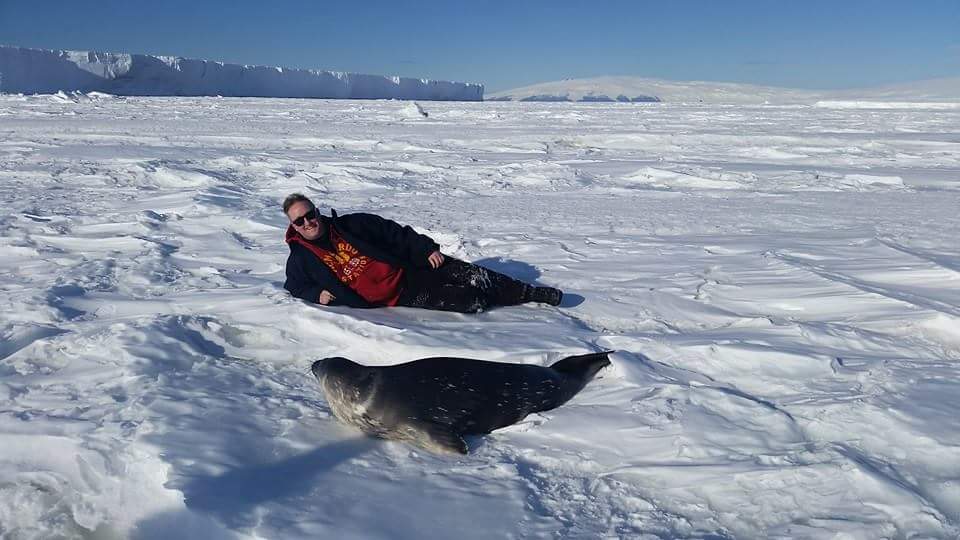 Justin Ramey laying on ice with a seal in front of him.